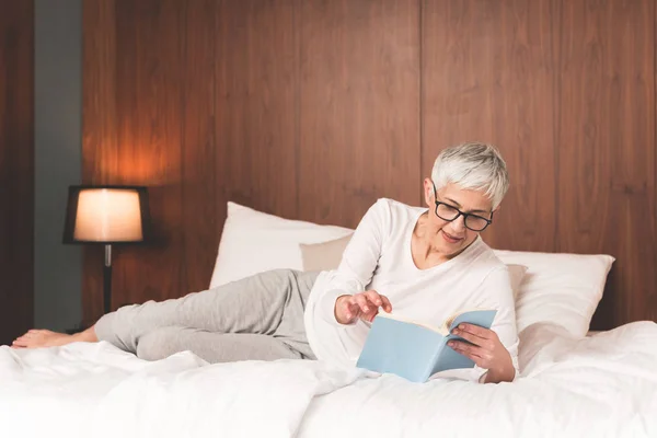 Зрелая Женщина Очках Лежащая Удобной Кровати Читающая Книгу — стоковое фото