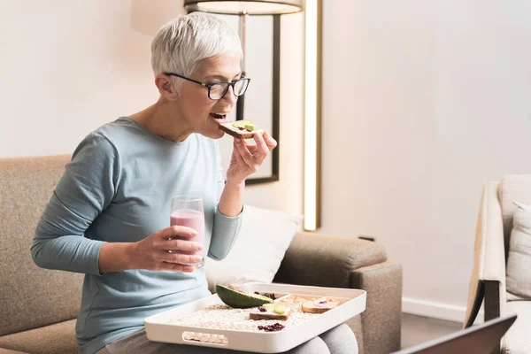 senior woman with glasses full of energy eating healthy toast with avocado and fruit yogurt
