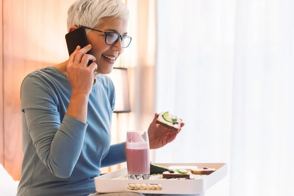 Mujer Mayor Alegre Hablando Por Teléfono Móvil Desayunando Sano Mañana —  Fotos de Stock