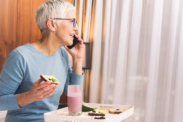 Joyful Senior Kvinna Talar Mobiltelefon Och Äta Hälsosam Frukost Ljusa — Stockfoto