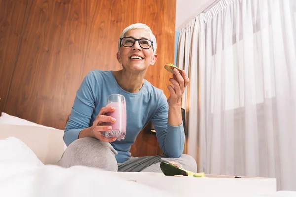 ゴージャスな熟女はアボカド 栄養価の高い完全菜食主義者食事概念と健康的なトーストを食べる眼鏡 — ストック写真