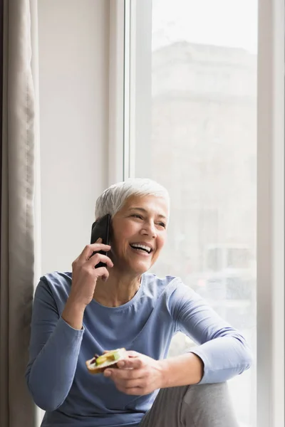 Wanita Senior Dengan Senyum Cantik Besar Berbicara Telepon Oleh Jendela — Stok Foto