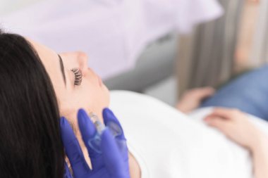 Hasta yanaklarında dolgu maddesi enjekte eden kadın doktor elinin yakın çekim 