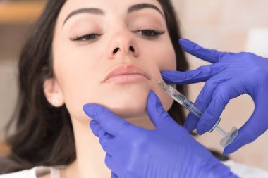 Close up of doctors hands injecting filler in upper lip of patient  clipart
