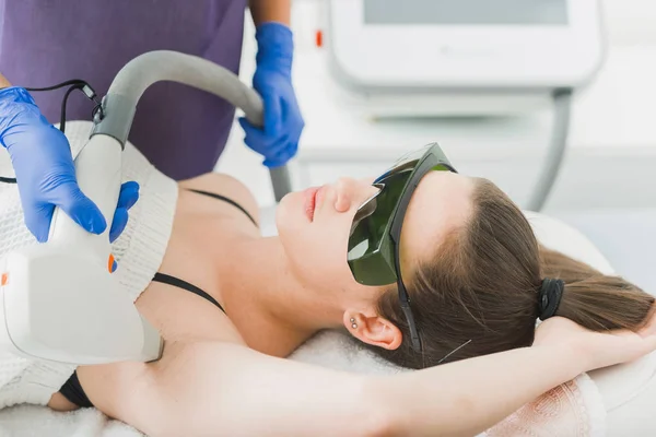 Woman having laser hair removal from underarm in dermatology center