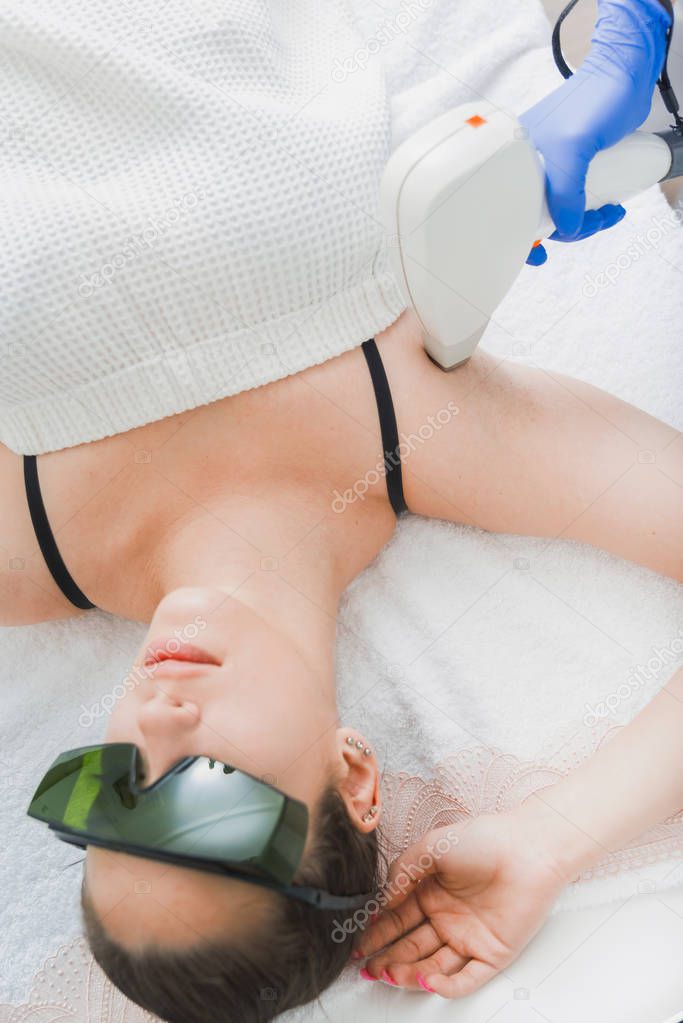 view of female patient with protective glasses having laser hair removal procedure on armpit