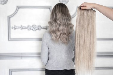 Kadın el saç uzatma örneği tutan ve arka planda sarışın ombre saç modeli ile kız ayakta