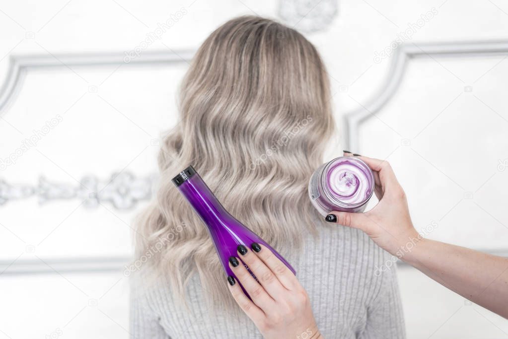 Female hands holding cosmetic products for colored hair, Back view of blonde with ombre hairstyle 