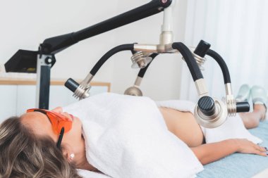 Kadın uzanıyor ve güzellik estetik kliniğinde modern lazer tedavisi görüyor. 