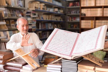 Baghdad, Iraq - July 06, 2019: Quran holy book of Muslims, Old man with big book clipart