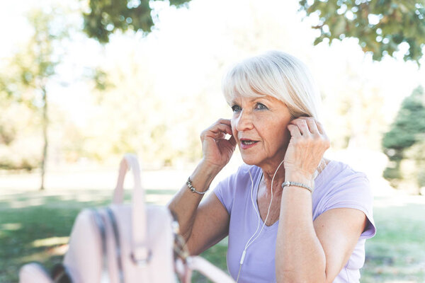 Senior lady putting headset in ears for listening music at park