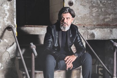 Terk edilmiş salonda eski merdivenlerde oturan yakışıklı manken.