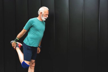 Kıdemli sporcu egzersiz öncesi ısınmak için bacaklarını açıyor, sağlıklı yaşam tarzı konsepti.