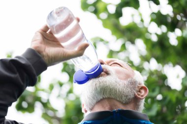 Kıdemli sporcu dışarıda egzersiz yaparken su içiyor, sağlıklı yaşam tarzı konsepti.