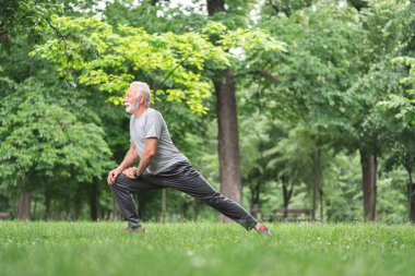 Yaşlı sporcu parkta esneme egzersizi yapıyor, sağlıklı yaşam tarzı konsepti.