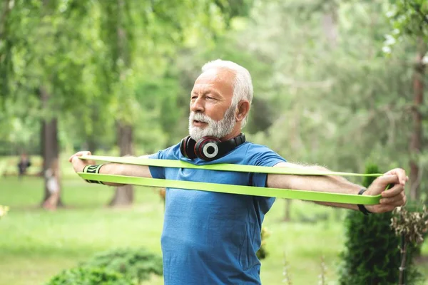Senior sportsman exercising with resistance band at park, healthy lifestyle concept