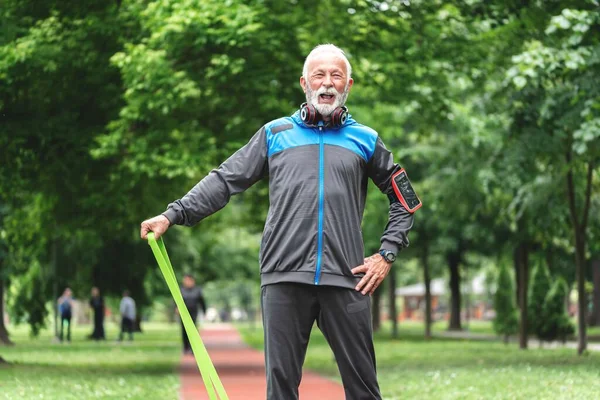 Senior sportsman exercising with resistance band at park, healthy lifestyle concept