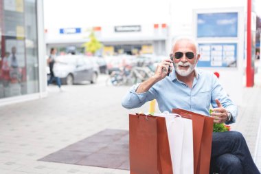Şehirde alışveriş yaptıktan sonra cep telefonuyla konuşan kıdemli adam, tüketim konsepti 
