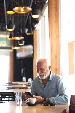 Kafede cep telefonu kullanan kıdemli bir adam, teknoloji kavramı.