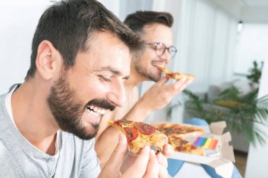 Gay couple enjoying pizza at home clipart