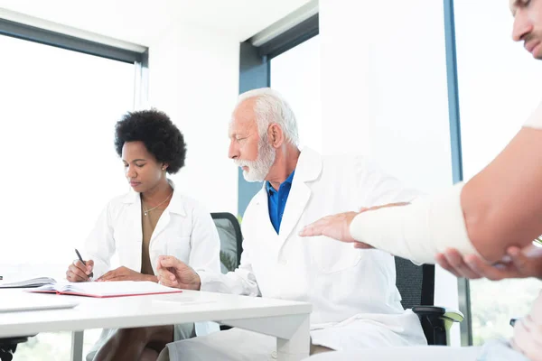 Doctor Studying Arm Injury Patient Assistant Writing Notes — Stockfoto