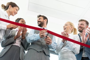 İş adamları yeni ofiste kırmızı kurdele keserken el çırpıyor