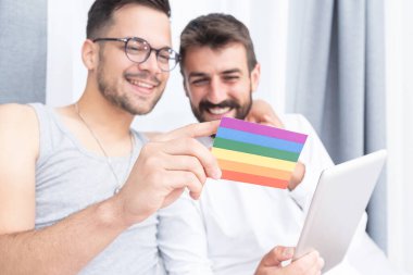 Yatakta lgbt renkli bayrağa bakan mutlu eşcinsel çift