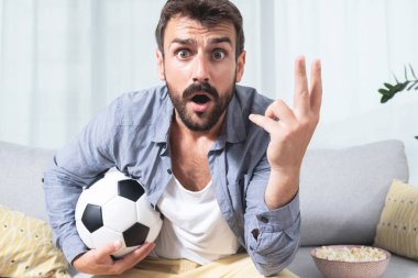 Şok olmuş suratlı genç adam futbol turnuvasını izliyor.