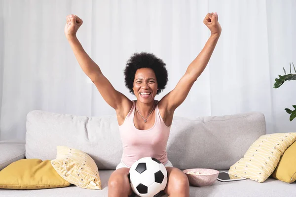 African American woman with winning gesture while watching football match in living room