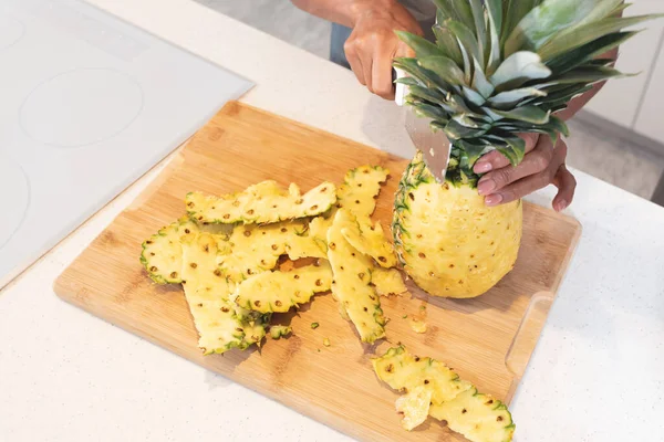 Hand of woman peeling pineapple fruit on cutting board in kitchen