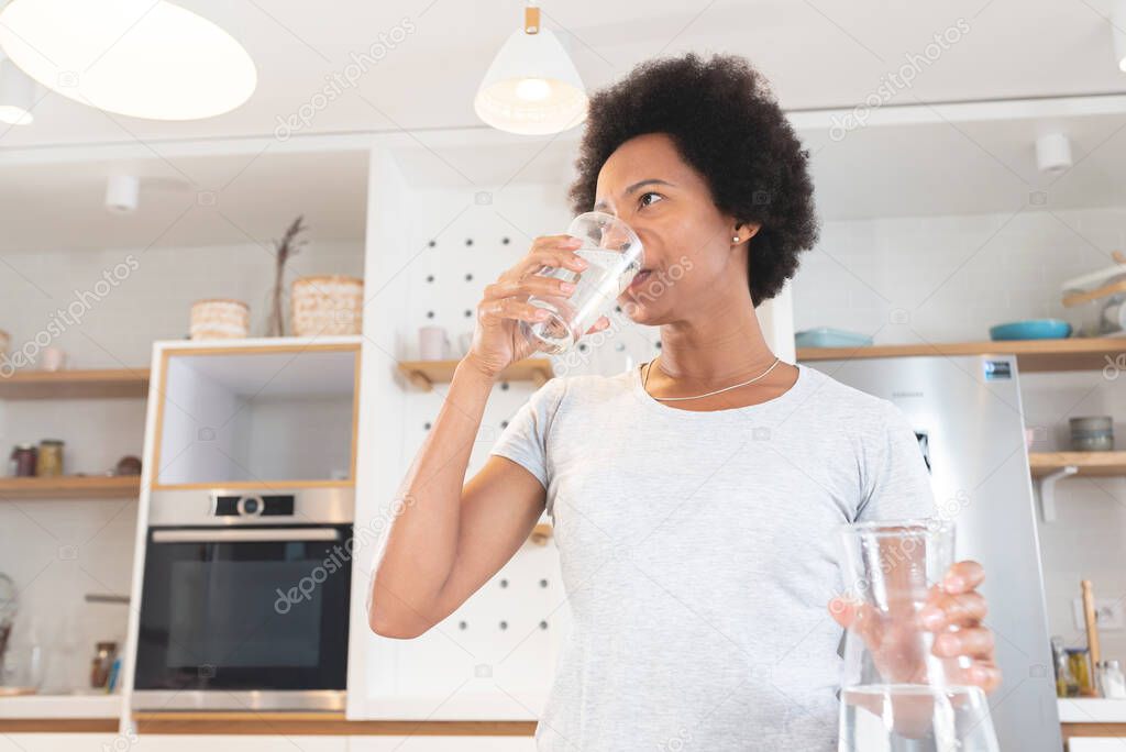 African American woman drinking water from glass in kitchen