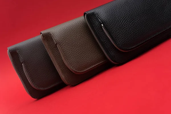 Different leather wallets on zipper. Red background. Close up view. Black, grey and brown wallet. Stock photo.
