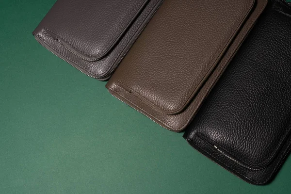 Different leather wallets on zipper. Green background. Close up view. Black, brown and green wallets. Stock photo.