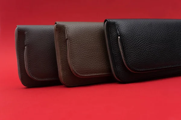 Different leather wallets on zipper. Red background. Close up view. Black, grey and brown wallet. Stock photo.