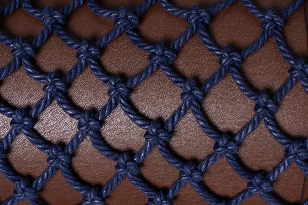 Luxury brown leather covered with blue rope net. Beautiful background. Closeup.