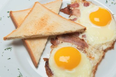 İştah açıcı kızarmış yumurta tost ve pastırma ile beyaz tabakta yeşillik ile dekore edilmiştir. Besleyici kahvaltı. 