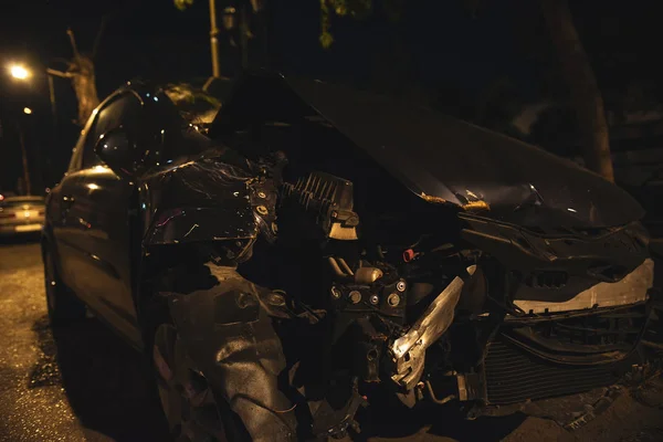 Destroyed car after a crash accident. The car is on the road in night city with low lights.