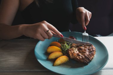 Kız turkuaz tabaktabaktabak üzerinde bıçak ve çatal ile sulu ızgara hindi biftek keser. Tavuk filetosu. Biftek karamelize şeftali ile servis.