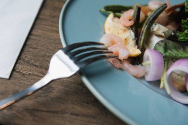 Üzerinde karides saplanmış bir çatalın yakın akrabası. Tahta bir masada karidesli lezzetli salata. Çatalüzerinde karides.