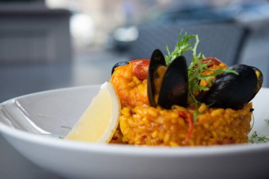 Midye ve karides limon ve arugula ile süslenmiş İspanyol paella. Beyaz bir tabakta servis edilir. Bokeh ile yakın çekim. Ana pirinç yemeği. Restoranda.