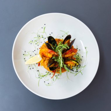 Midye ve karides limon ve arugula ile süslenmiş İspanyol paella. Gri bir masada limon ile beyaz bir tabak tabaktabak tabaktabak tabaktabak tabaktabak tabaktabak tabaktabak tabaktabak tabaktabak tabaktabak tabaktabak tabaktabak tabaktabak tabaktabak tabaktabak tabaktabak Yukarıdan görüntüleyin. Kare fotoğraf.