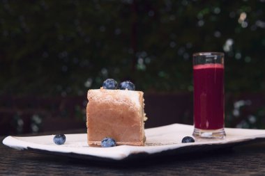 New York cheesecake ve yaban mersini. Kahverengi kabuklu lezzetli bir turtadan bir dilim. Bir bardak ahududu sosu ile servis edilir. Bokeh ve kopyalama alanı ile yakın çekim.