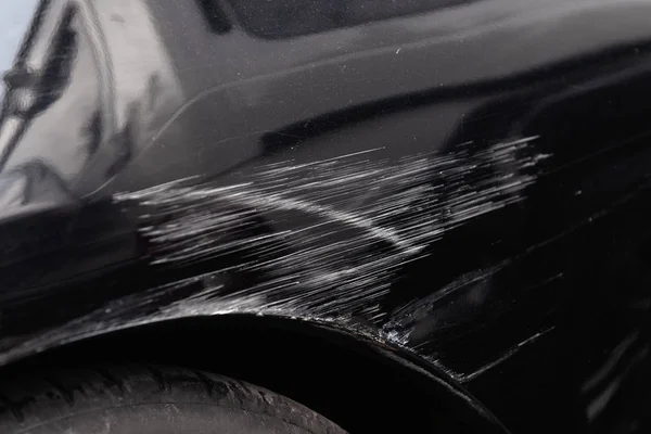 Damaged car body after a crash accident. Black vehicle wheel arch closeup. Scratches and dents. Repairs needed.