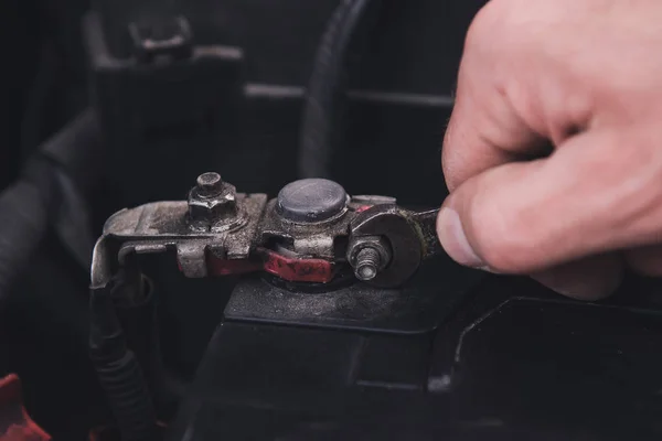 Man\'s hand tightens the nut with an old wrench. Battery replacement at the garage. Closeup.