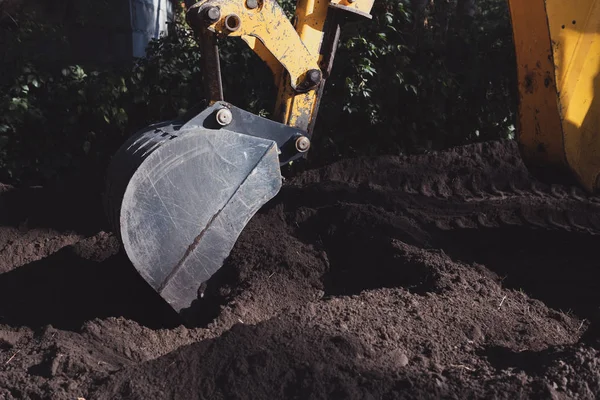 在阳光明媚的日子里 黄色的挖掘机铲斗正在黑地上挖一个洞 施工期间的工程机械 — 图库照片