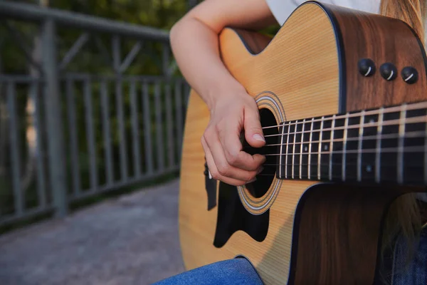 Girl\'s hand plays the acoustic guitar. Young musician making money on the bridge. Street music concept. Closeup.