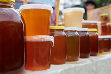 Markette bir sürü farklı bal çeşidi olan kavanozlar. Masada ev yapımı sağlıklı ürünler var. Amber, turuncu ve kahverengi sıvılar. Arıcı işi..