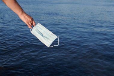 Denize karşı kızın elindeki koruyucu mavi yüz maskesi. Coronavirus konsept fotoğrafının iyileşmesi. Boş alan. Salgının sonu.