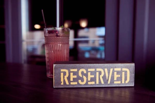 Metal reserved sign in the restaurant against beautiful cocktail. Table reserve concept photo.