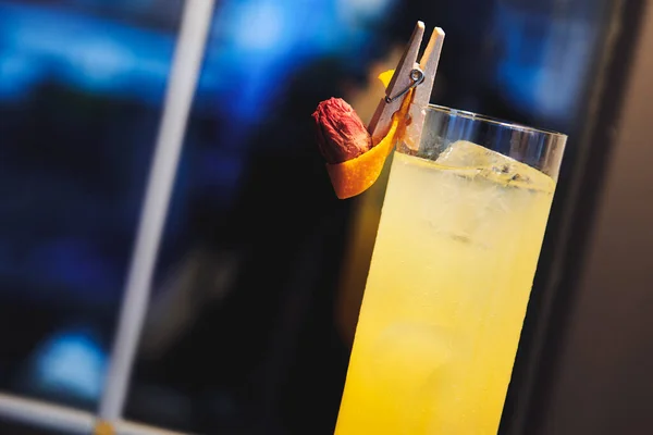 Beautiful yellow alcohol cocktail in wineglass near the window in the bar. Drink decorated with wooden pin dry rose and orange.  Ladies drink. Copy space for text. Closeup.